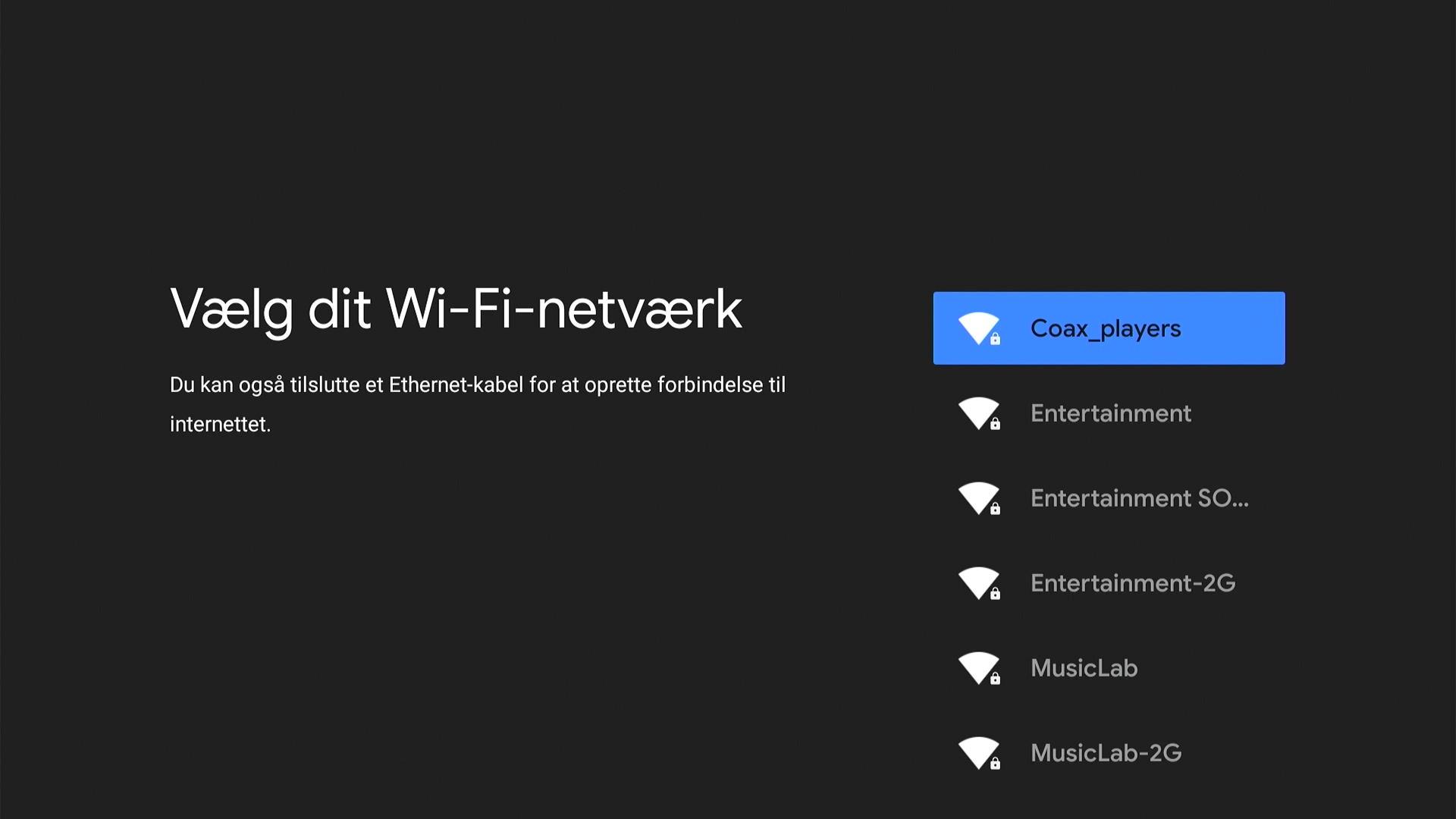 Skærmbillede af YouSee‑opsætningsskærm med overskriften “Vælg dit Wi‑Fi‑netværk” og en liste over trådløse netværk, hvor ét netværk er markeret med en blå farve. Mørk baggrund.